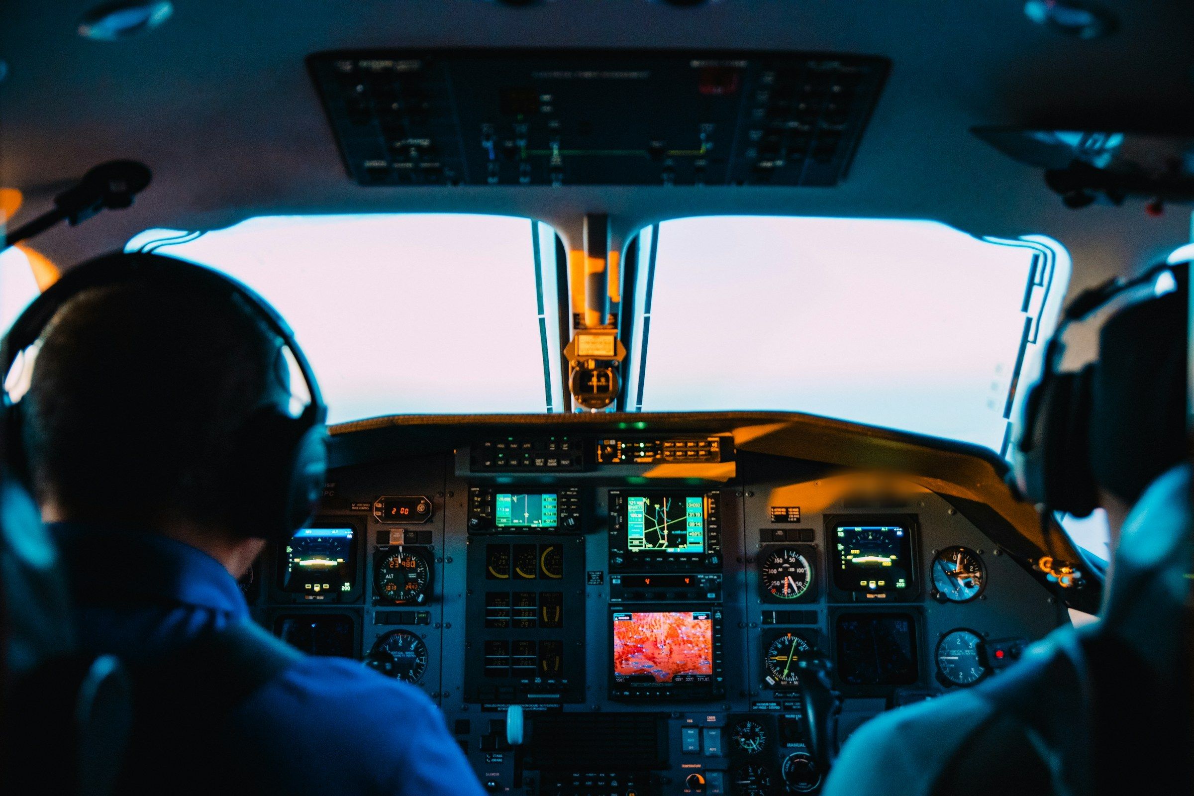 Dos pilotos de espaldas en la cabina, frente al parabrisas iluminado