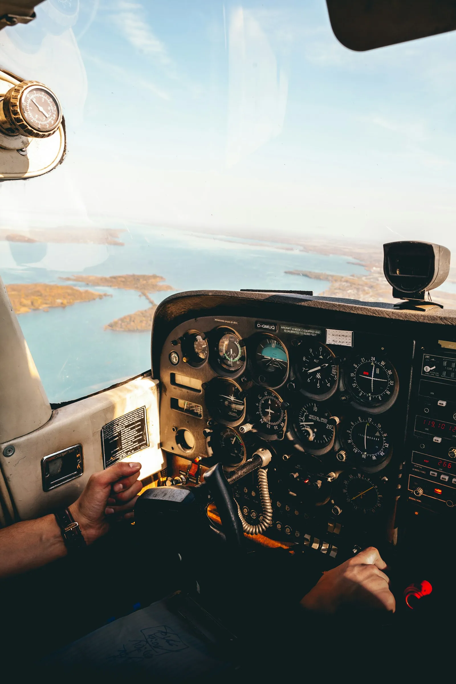 Manos de un piloto en los mandos de una avioneta, con el mar y la costa al otro lado del parabrisas