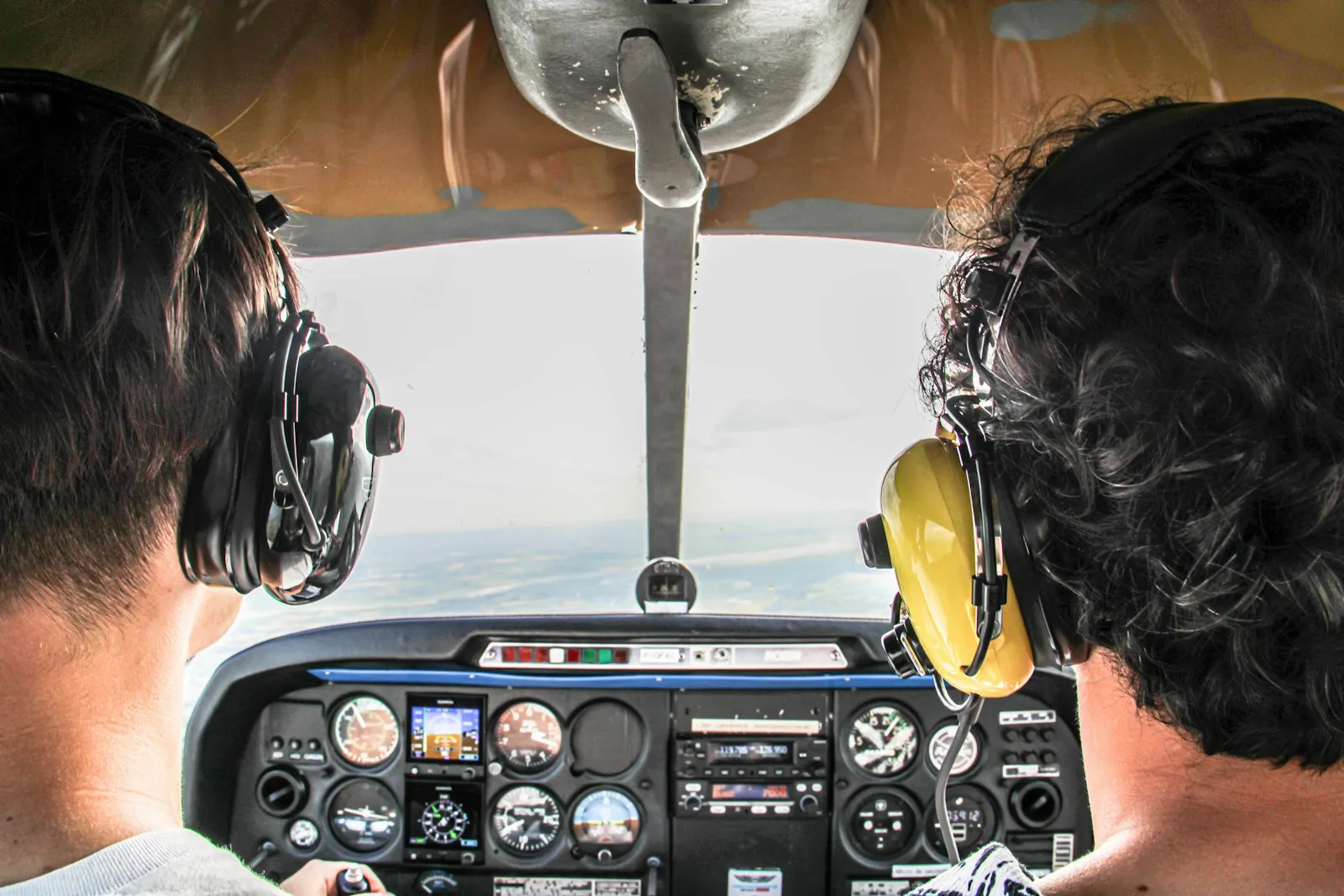 Instructor y alumno con auriculares en la cabina, volando sobre las nubes